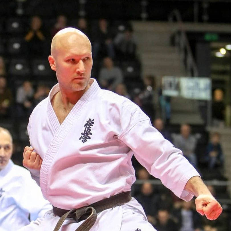 Person in a martial arts uniform performing a move in an indoor setting with spectators.