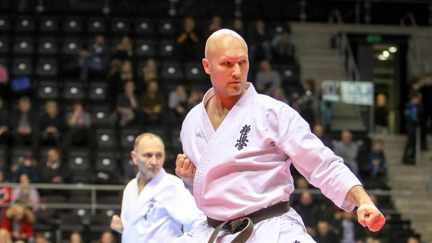 Person in a martial arts uniform performing a move in an indoor setting with spectators.